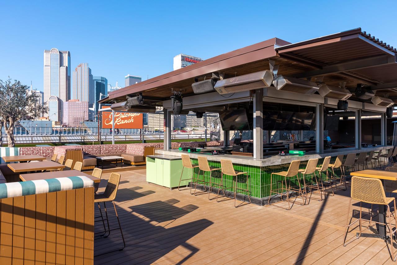 Outdoor rooftop bar with green-tiled counter, modern barstools, and the Dallas skyline in the background on a clear day.