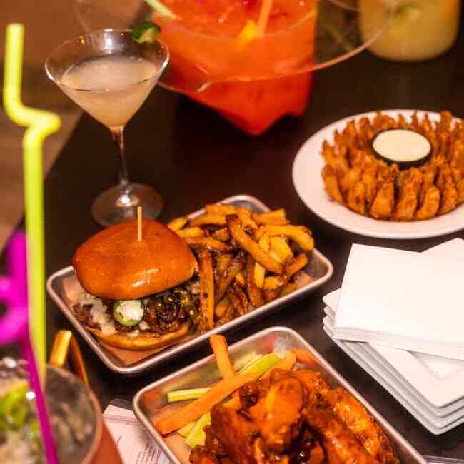 Close-up of a table with a burger, fries, chicken wings, celery sticks, a martini, and a blooming onion appetizer.
