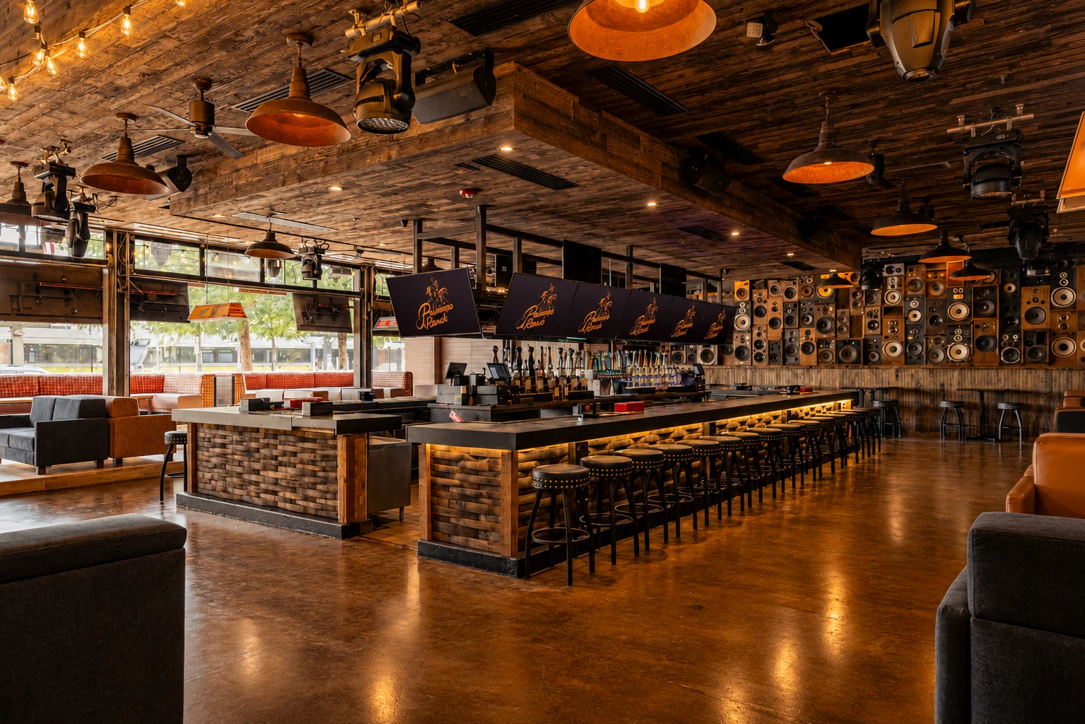 Wide-angle view of a Western-themed bar interior featuring wood-paneled ceiling, exposed beams, barstools, and vintage signage along the walls.